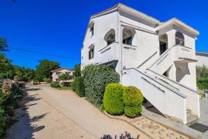 un edificio bianco con arbusti verdi accanto a un marciapiede di Apartment Dragica a Malinska