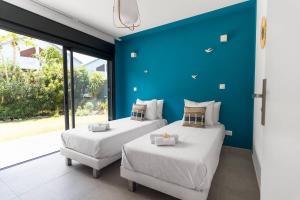 two beds in a room with a blue wall at VILLA Ô 3 CAP - Magnifique Villa - classée 4 étoiles - Piscine CHAUFFEE - 4 ch - 8 personnes - accès direct à la plage et à l'esplanade de BOUCAN CANOT in Saint-Gilles les Bains