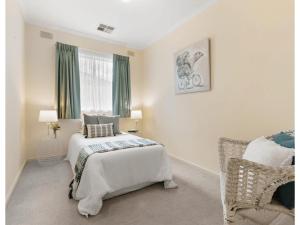 a white bedroom with a bed and a chair at 3BR Guest House near Adelaide CBD Joslin 5070 in Evandale