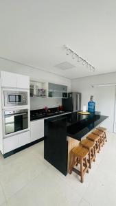 une cuisine avec des appareils électroménagers noirs et blancs et des tabourets en bois dans l'établissement Casa com piscina - Costa do Sol, à Bertioga