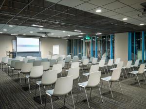a conference room with white chairs and a screen at Tulip Inn Eindhoven Airport in Eindhoven