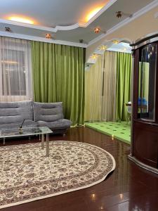 ein Wohnzimmer mit einem Sofa und grünen Vorhängen in der Unterkunft 38 Теплые апартаменты с 2 кроваями у Байтерека in Zhezdi