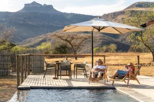 two people sitting under an umbrella next to a pool at Sasi Bush Lodge- Exclusive Use Luxury Tented Safari Lodge in Bergville