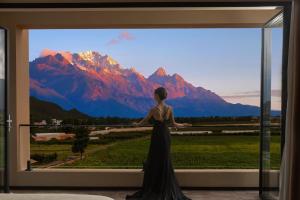 a woman standing in front of a window with a mountain view at ShanJuanYun Panoramic Sunlit Yulong Snow Mountain Hotel in Baisha
