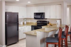 a kitchen with white cabinets and a black refrigerator at Wyndham Ocean Walk Resort 2BR Apartment with Resort Access in Seabreeze