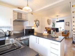 a kitchen with white cabinets and black counter tops at Periwinkle Cottage in Conwy