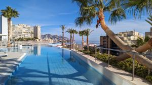 a swimming pool with palm trees and the ocean at SUNSET CLIFFS fantastic apartment in Benidorm
