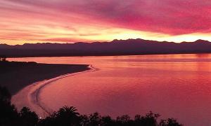 una puesta de sol sobre un cuerpo de agua con montañas en Beach side Apartment Nelson, en Nelson