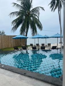 a swimming pool with chairs and umbrellas and the ocean at ThreeTreesSamuiPoolVilla in Ban Thung