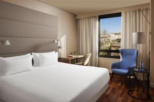 a hotel room with a white bed and a blue chair at NH Sevilla Plaza de Armas in Seville