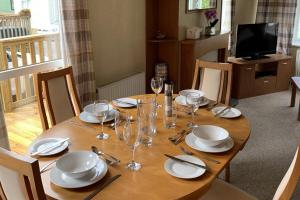a wooden table with plates and wine glasses on it at 2 Bed Caravan - Sleeps 6 - Pets - River Teviot in Hawick +4 photos