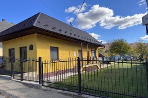a yellow house with a black roof behind a fence at Vila Andrássy in Vlachovo