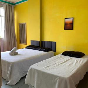 two beds in a room with yellow walls at Quarto vista mar in Rio de Janeiro