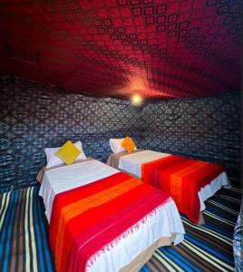 two beds in a room with red and colorful sheets at ERG MERZOUGA SAHARA CAMP in Merzouga