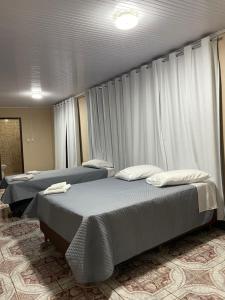 two beds in a room with white curtains at Hotel Diplomata in Tupanciretã +6 photos