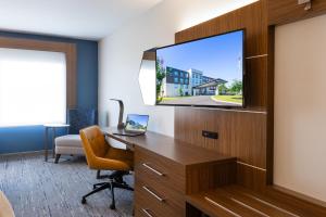 a hotel room with a desk and a tv on a wall at Holiday Inn Express & Suites Greenwood Mall by IHG in Greenwood