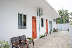 a white building with two benches and a red door at Shadow Isles Himandhoo in Himandhoo 