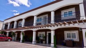 un edificio blanco con balcones y un coche rojo aparcado delante en Hotel Rincon Real Suites, en Durango