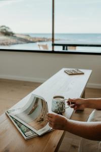 a person sitting at a table with a cup of coffee at Stones Throw - Brand New Beach House in Stokes Bay +116 photos