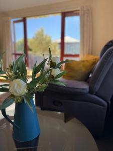 eine blaue Vase mit Blumen auf einem Tisch mit einer Couch in der Unterkunft Seaview Akaroa in Akaroa