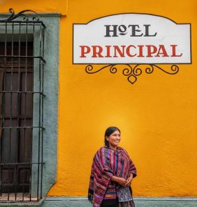 une femme debout devant un bâtiment jaune dans l'établissement Hotel Principal, à Oaxaca