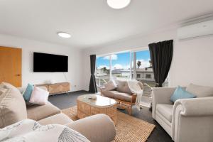 a living room with couches and a flat screen tv at Ohope Ocean Breeze Escape in Ohope Beach