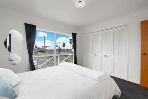 a bedroom with a white bed and a large window at Ohope Ocean Breeze Escape in Ohope Beach