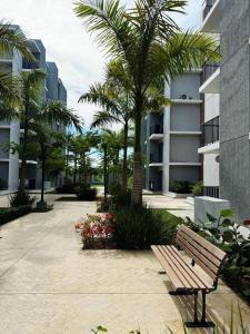 a park bench in front of a building with palm trees at Jardines III LAUREL 302 in Punta Cana +2 photos