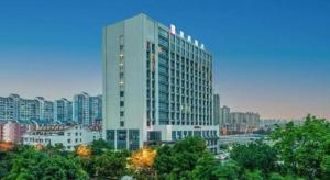 a tall white building with trees in front of a city at Echarm Hotel Liuzhou Liunan Wanda Plaza in Liuzhou