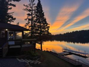 a cabin on a lake with a sunset in the background at Private 6-Bdrm Lodge on 1000ft Sandy Lakeshore in Round Lake Seaplane Base