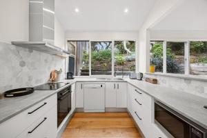 a white kitchen with white cabinets and windows at Heath Cliff House in Aireys Inlet