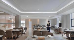 a man standing in a room with tables and chairs at Vienna Hotel Zhejiang Tongxiang Puyuan in Puyuan