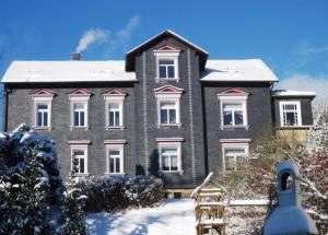 Una gran casa gris con nieve en el suelo en Elegante Ferienwohnung mit Kaminofen im Thüringer Wald, en Manebach