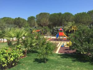 トッレ・サンタ・サビーナにあるCamping Cala dei Ginepriのヤシの木や茂みのある公園内の遊び場