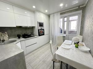 a kitchen with white cabinets and a table with flowers on it at Sky Apartment Bolashak in Aktobe
