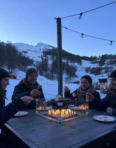 een groep mensen die rond een tafel met vuur zitten bij Hôtel Chalet Sainte-Anne in Condamine-Châtelard