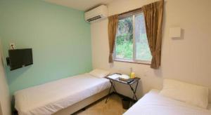 two beds in a room with a window and a table at Rich Reson ISHIGAKI in Fukai