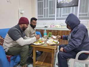 a group of three men sitting around a table eating food at TN's Basecamp Hostel in Tawang