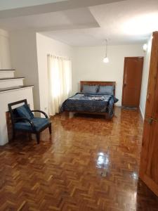 a bedroom with a bed and a chair on a wooden floor at Kodai ARYASREE in Kodaikānāl