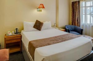 um quarto de hotel com uma cama e uma cadeira e uma janela em New Ambassador Hotel em Harare