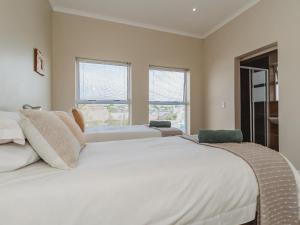 a white bedroom with two beds and two windows at Manor One Kingswood Golf Estate in George