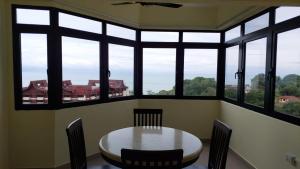 einen Tisch und Stühle in einem Zimmer mit Fenstern in der Unterkunft Batu Ferringhi Luxury Seaview Suite - 3Br in Batu Feringgi