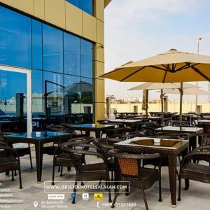 an outdoor patio with tables and chairs and an umbrella at Bristol Hotel Salalah in Salalah