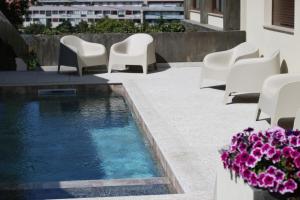 a swimming pool with white chairs and purple flowers at ma-la studios Guimarães in Guimarães