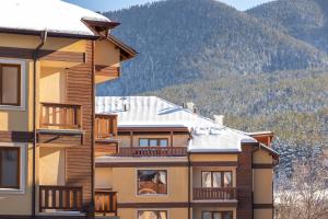 un bâtiment avec un toit couvert de neige avec des montagnes en arrière-plan dans l'établissement Pirin Sense Apartment Complex, à Bansko