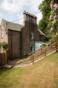 an old brick house with a fence in front of it at Glen Lodge And Abhainn Cottage By Birch Stays in Stonehaven