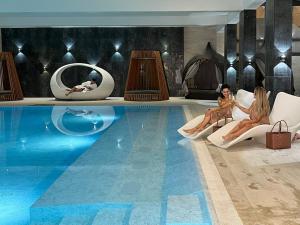 deux femmes assises sur des chaises à côté d'une piscine dans l'établissement Resort Hotel Sonnenhof Grafenau, à Grafenau
