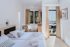 a white bedroom with a large bed and a balcony at Paradise Hotel-Apartments in Stalida