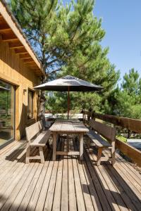 einem Holztisch mit einem Regenschirm und Bänken auf einer Terrasse in der Unterkunft Cabaña Meliades - Bosque & Calma en Familia - Ayres Del Bosque Alojamientos in Ostende