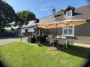 a table and chairs under an umbrella in front of a house at La Maison d'hôtes LA PUYERRE in Hours